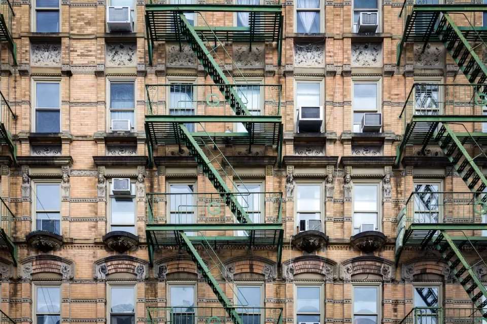 Brick New York City apartment building exterior with fire escape stairs and AC window units.